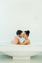 Obraz na płótnie Canvas brunette woman hugging handsome shirtless man in bathtub