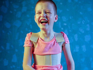 Kid in corrector for spine in pink t-shirt on a gray background .Child wearing back support belt for support and improve back posture
