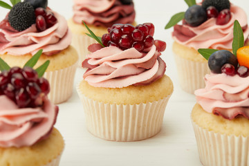 selective focus of cupcakes with cream and berries on white surface