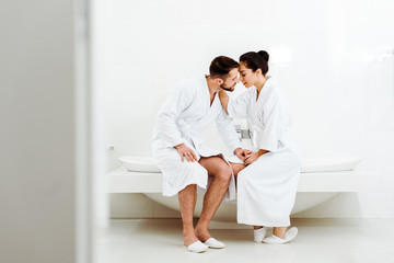 selective focus of bearded man sitting and holding hands with attractive girl in bathrobe