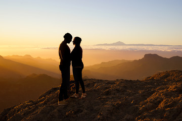 young kissing couple standing on mountain in front of golden sunset - silhouettes, gran canaria and tenerife