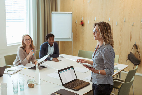 Confident businesswoman discussing with colleagues in meeting at office