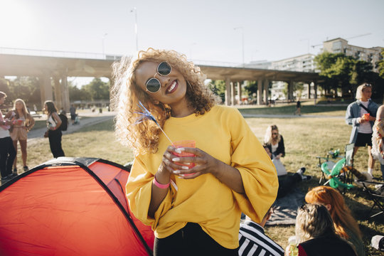 Portrait of smiling woman with drink standing against friends at musical event in summer