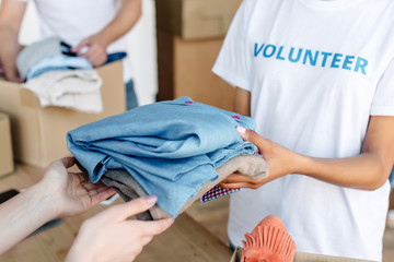 cropped view of volunteer giving clothes to woman in charity center