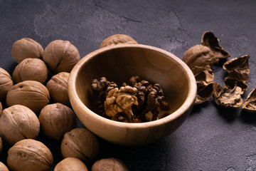 Walnut kernels in wooden bowl and whole walnuts on blue slate surface. Healthy nuts and seeds composition.