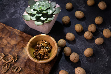 Obraz na płótnie Canvas Walnut kernels in wooden bowl, whole walnuts and Echeveria plant on blue slate table. Healthy nuts and seeds composition.