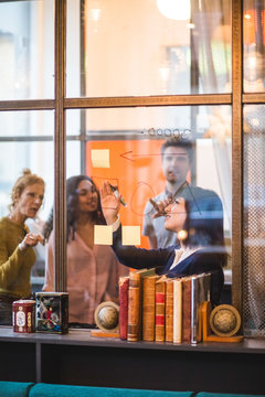 Confident businesswoman planning strategy on glass wall with colleagues at creative office