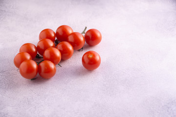 Bunch of cherry tomatoes on white textured stone concrete table, side view with copy space. Ingredients for cooking.