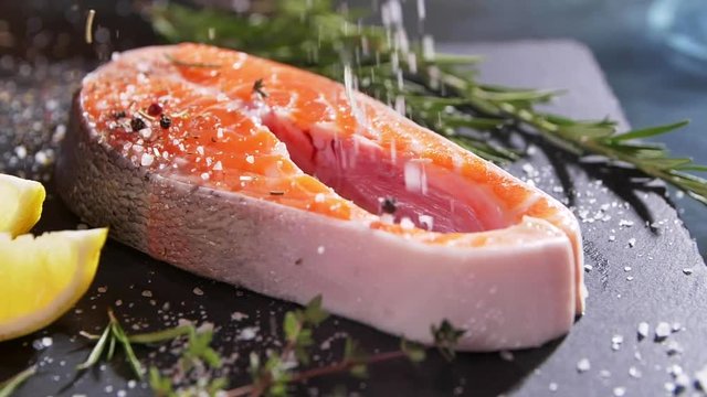 Close up rotation view of seasoning process of salmon&rsquo;s fillet. Spicing with salt, pepper, rosemary. European cuisine, delicious taste, professional cooking. Slow motion