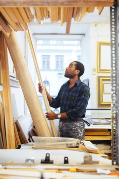 Confident young craftsman holding at timber in framing workshop