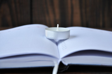 open notepad lying on a wooden table. There is a small candle on the notebook. The background is pinkish.