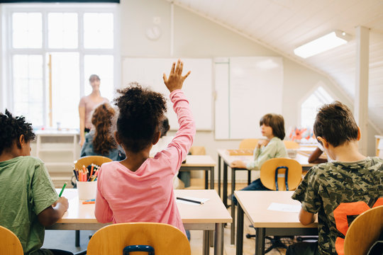 Rear view of boy raising hand while answering in class at elementary school