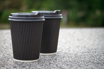Two black disposable cups of coffee with lids are standing on the stone parapet