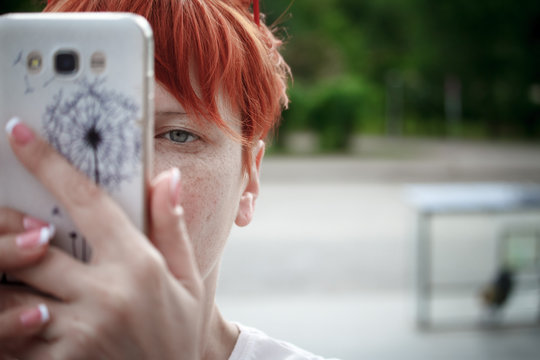 Close-up of a young woman with short red hair walking around the city, taking pictures on a mobile smartphone