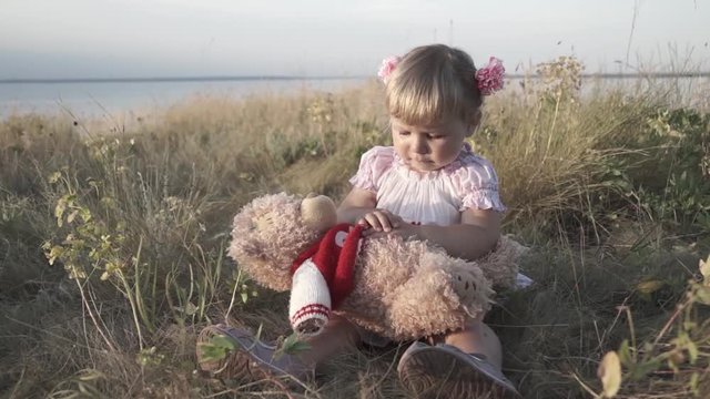 Little girl playing in the field. Teddy bear.