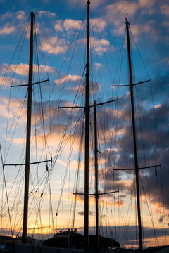 Sailing ship masts and rigging against a cloudy sky at sunset.