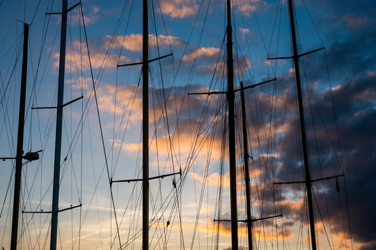 Sailing ship masts and rigging against a cloudy sky at sunset.