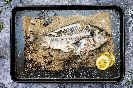 High angle close up of skeleton of grilled sea bream on baking tray.
