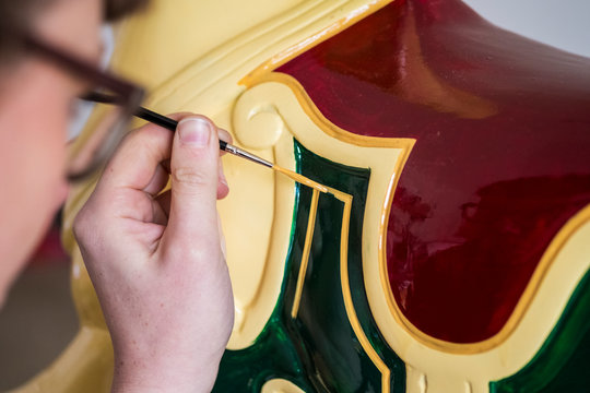Close up of woman wearing glasses in a workshop, painting traditional wooden horse from merry-go-round.,Signwriter