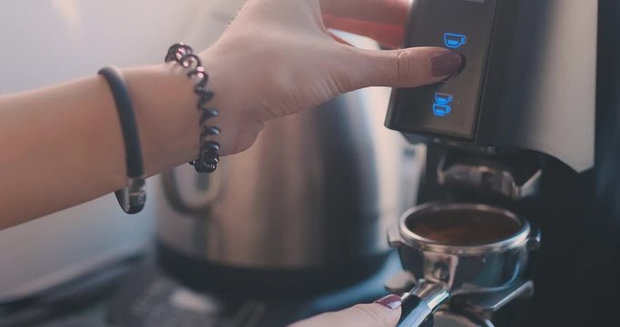 Selected focus on the hands of professional barista pushing the button and holding the handle of the coffee machine