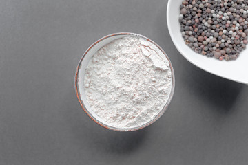 Round bowl full of white flour, bowl with spices, peppercorns, near on black background. Top view, flat lay. Natural light. Copy space. Horizontal image.