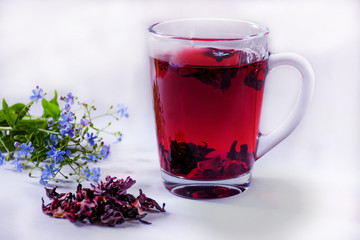 A mug with red hibiscus tea and a branch of blue flowers