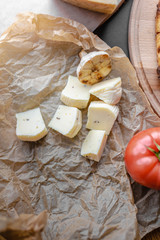 Cheese pieces with fried half of garlic and tomato on white cooking paper with tomatoe and wooden cutting board. Top view, flat lay, black background, copy space.