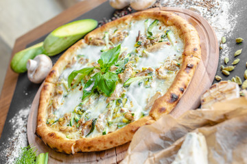 Pizza with zucchini, meat, cream cheese on the table in the restaurant. Onion, zucchini, champignons and spices near on the table, piese of cheese. Horizontal image. Natural light. Black background. 