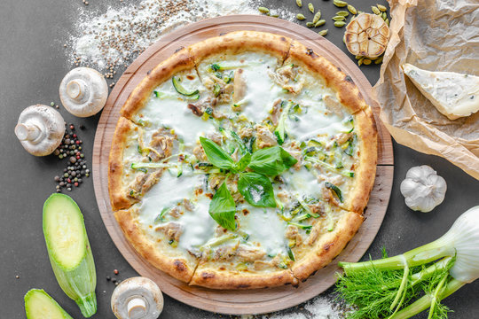 Pizza with zucchini, meat, cream cheese. Pepper, zucchini, champignons, garlic,  onion and piece of cheese next to the table. Horizontal image. Top view, flat lay. Natural light. Black background. 