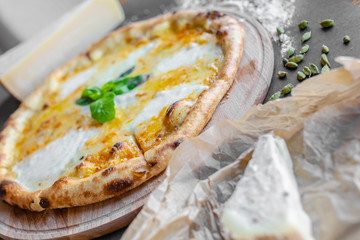 Pizza with four kinds of cheese on the table in the restaurant. Spices and different cheese near. Horizonal image. Natural light. Black background. 
