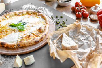 Pizza with four kinds of cheese on the table in the restaurant. Spices, tomatoes  and different cheese near. Horizonal image. Natural light. Black background. 