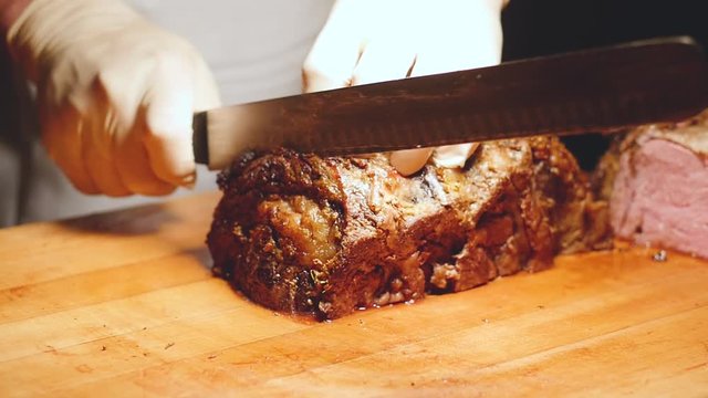 man slices prime rib in slow motion as camera circles. Close up slow motion shot as a chef uses big knife to cut prime rib in the restaurant