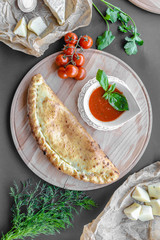 Traditional georgian pie with a bowl of tomato sauce on a wooden plate. Vertical image, top view, flat lay, copy space, black background.