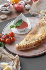 Traditional georgian pie with a bowl of tomato sauce on a wooden plate. Vertical image, black background.