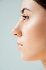 profile of young woman with shiny lips, highlighter and golden eye shadow isolated on grey