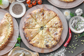 Georgian khachapuri pies with cheese and meat on the plate, red pepper, tomatoes, mushrooms, herbs, onion and bowls with spices nearby on the table. Horizontal image. Top view, flat lay.