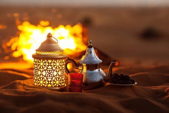 Dates, teapot, cup with tea near the fire in the desert with a beautiful background. Ramadan Kareem