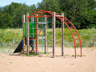 Beautiful colored children playground on the sand in the yard. Close-up of a colorful and multi-functional playground. Against the background of green grass and trees. Great pastime.