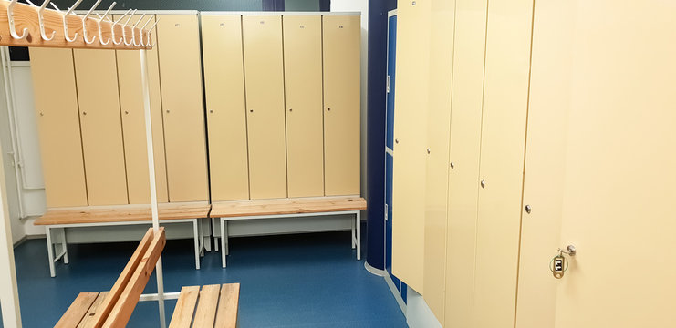Women or men dressing or changing room in the gym of the training complex. Row of steel lockers and wooden benches on the blue floor. The key inserted into the lock.