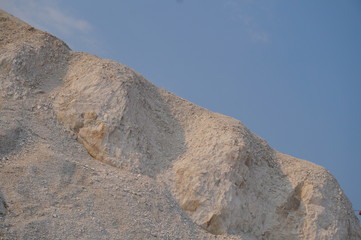 White chalk cliffs with rough splits on a blue sky background and blurred withered grass in the foreground