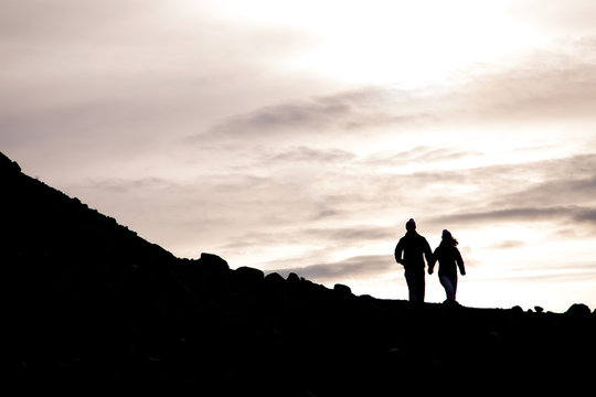 Silhouette of couple holding hands while walking on mountain at sunset