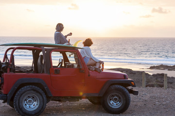 Two surfer girls with sunglasses on their 4x4 car drinking beer