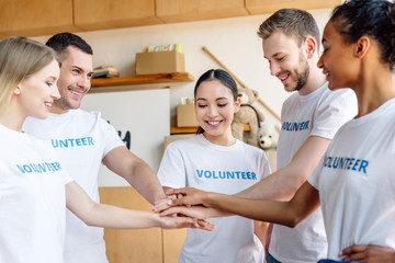 Obraz premium five young multicultural volunteers smiling and holding hands in charity center