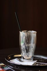 A tall empty glass Cup with a black straw after a coffee cocktail on a silver tray with a long spoon in the cafe.