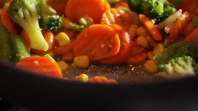 Close up view of colorful steaming vegetables frying on a pan being mixed and tossed up. Cooking process, healthy food, vegetarian cuisine. Delicious taste, homemade dish. Slow motion