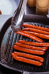 young woman in a gray apron fries sausages