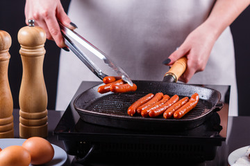 young woman in a gray apron fries sausages