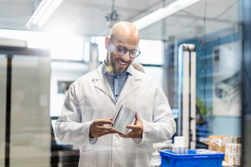 Smiling technician wearing lab coat examining workpiece