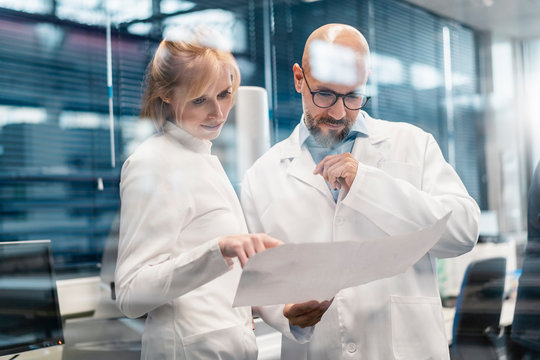 Two Technicians Wearing Lab Coats Looking At Plan