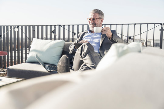 Smiling mature businessman with cup of coffee and tablet on roof terrace